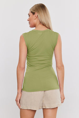 A person with long blonde hair is standing, facing away. They are wearing the ESTINA TANK TOP by Velvet by Graham & Spencer in green and beige shorts.