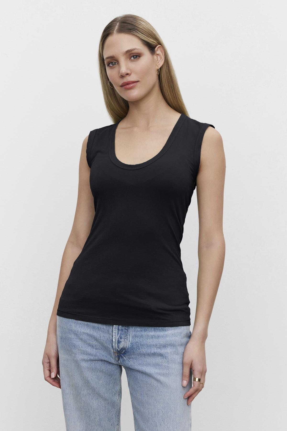   A woman with long hair wearing the ESTINA TANK TOP by Velvet by Graham & Spencer and blue jeans stands against a plain white background. 