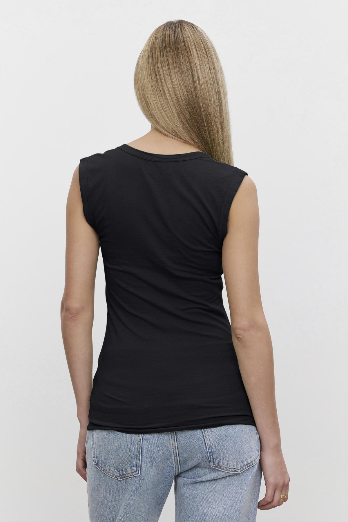   A person with long, straight hair is shown from the back, wearing a black ESTINA TANK TOP by Velvet by Graham & Spencer and light blue jeans against a plain white background. 