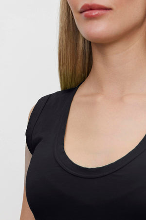 Close-up of a woman wearing a black ESTINA TANK TOP by Velvet by Graham & Spencer, showcasing the neckline and part of her face, with straight, light brunette hair against a plain background.