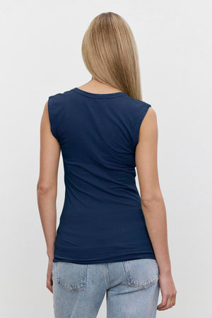 A person with long, straight hair in a Velvet by Graham & Spencer ESTINA TANK TOP and light blue jeans is standing and facing away from the camera.