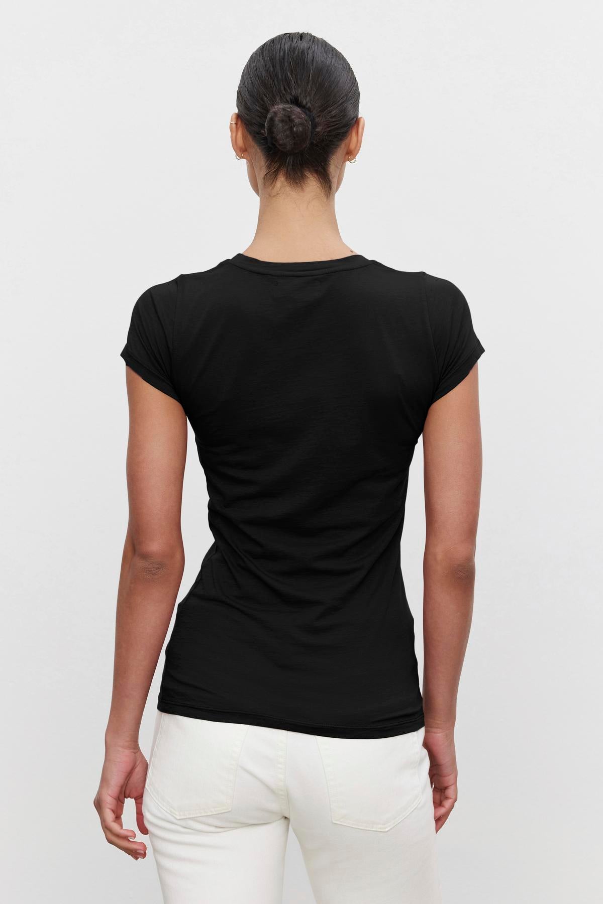   Person with hair in a bun wearing an ultra-soft gauzy whisper black JEMMA TEE by Velvet by Graham & Spencer and white pants, facing away from the camera. 