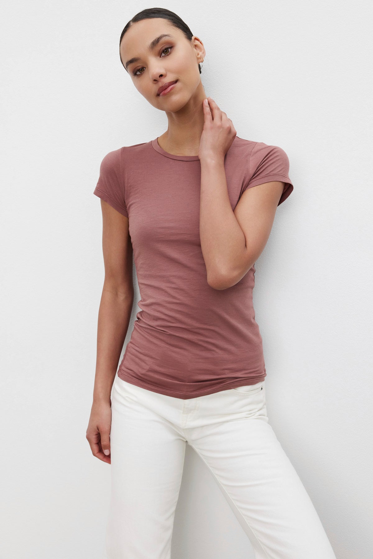 A person stands against a plain white background, wearing a JEMMA TEE by Velvet by Graham & Spencer and white pants, with one hand touching their neck.-37648673046721