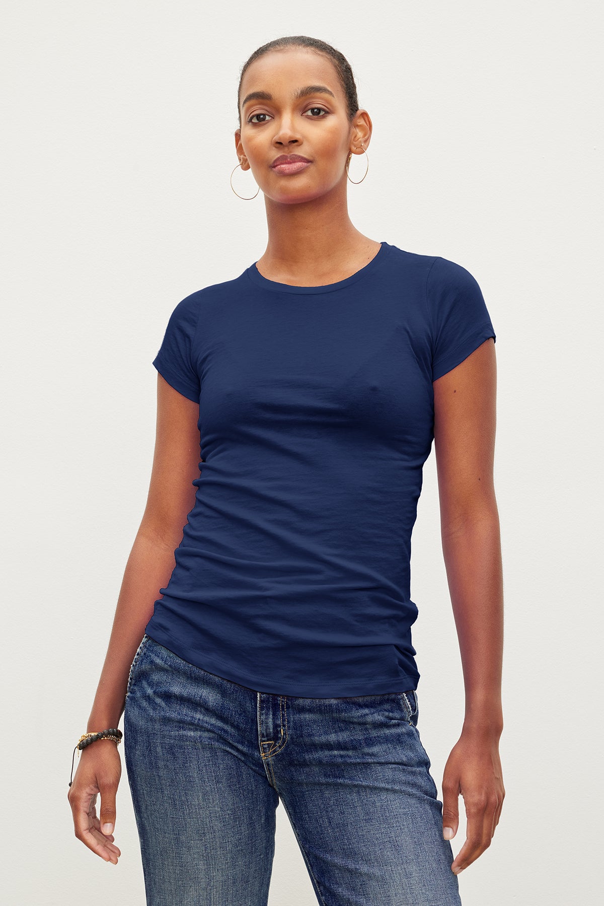   A person wearing a fitted crew neck navy blue JEMMA TEE by Velvet by Graham & Spencer and jeans stands against a plain background. 