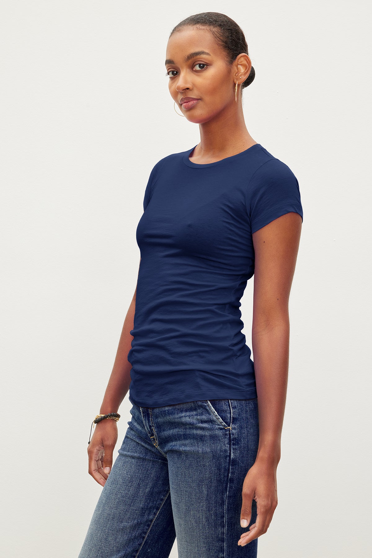   A person with short hair wears a fitted crew neck navy blue JEMMA TEE by Velvet by Graham & Spencer and blue jeans, standing against a plain background. 