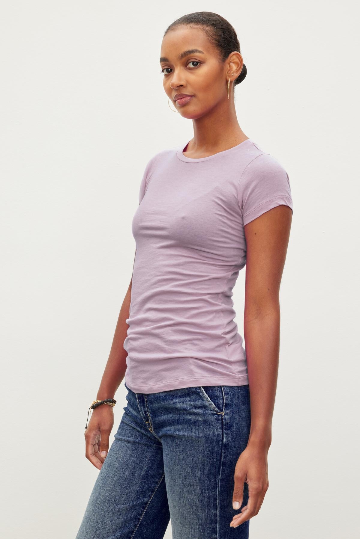 A woman with short hair wearing a light purple, ultra-soft gauzy JEMMA TEE by Velvet by Graham & Spencer and blue jeans, standing against a plain white background.-37241159647425