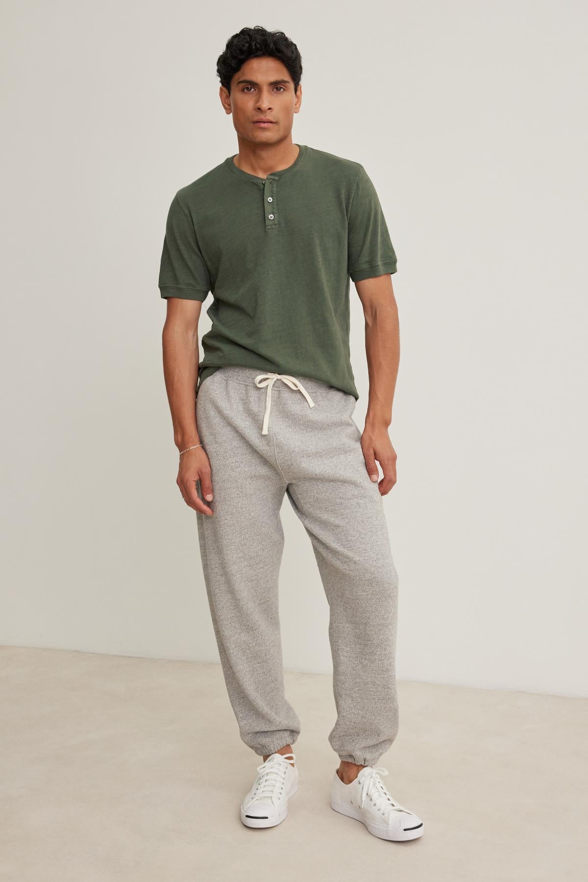 A man stands wearing a green henley shirt, Velvet by Graham & Spencer KEELAN JOGGER in gray, and white sneakers against a plain background.-38643388416193