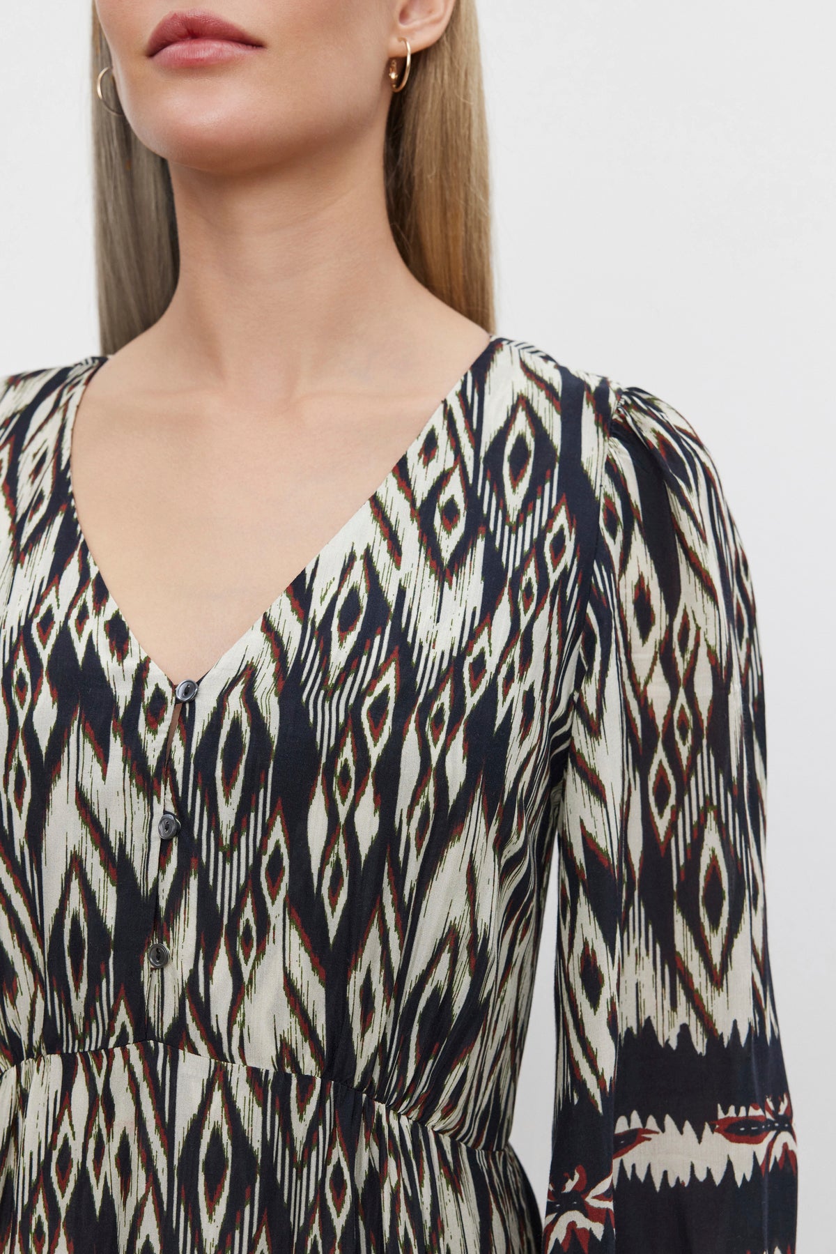   A person is wearing the CATHERINE DRESS by Velvet by Graham & Spencer, featuring a black and white ikat print with long sleeves and a V-neckline. The image captures the upper torso and part of the face, though the spotlight is on the dress's design. 