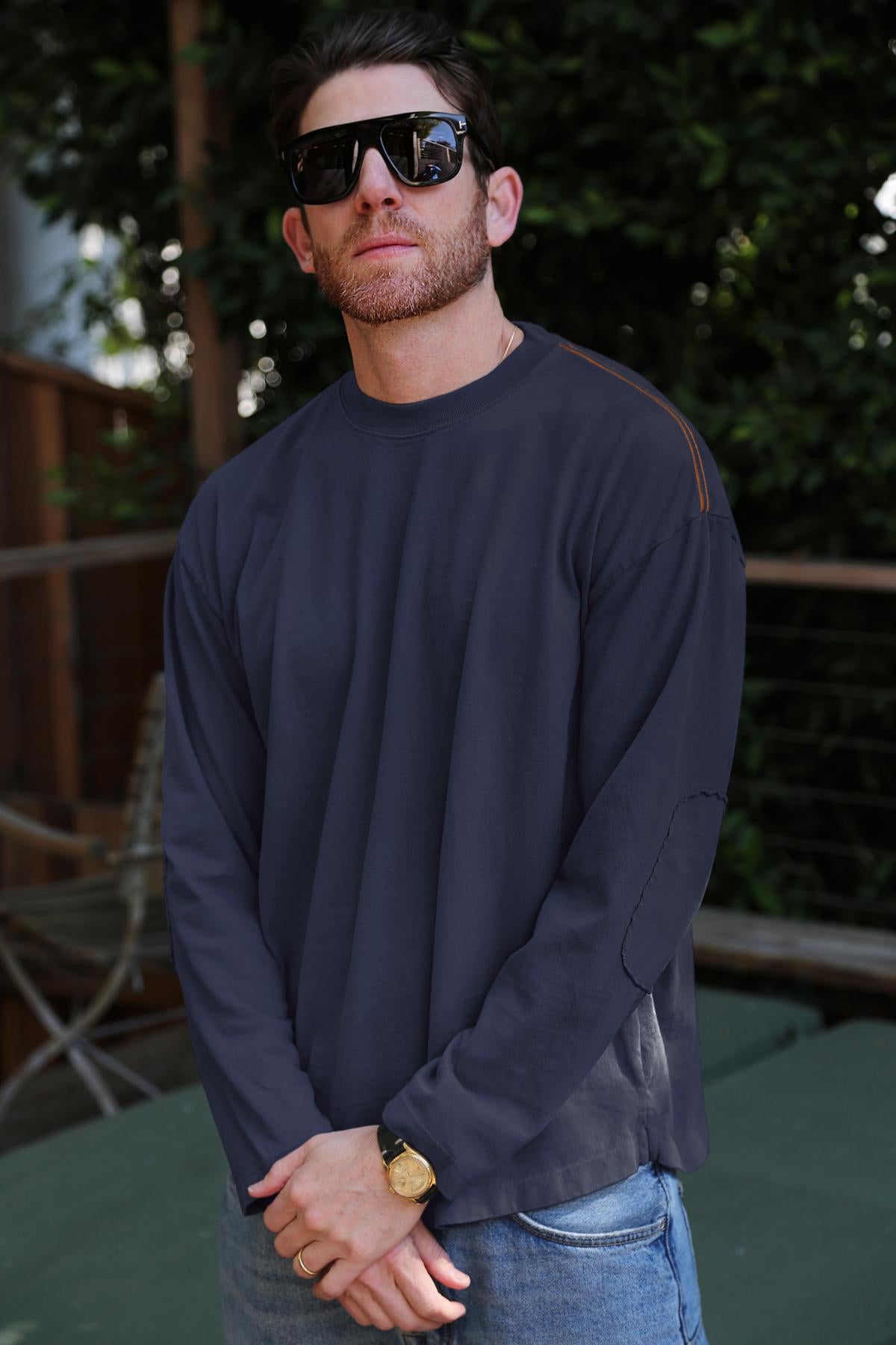 A man with a beard and sunglasses stands outdoors, sporting the SLATER TEE in a relaxed fit and structured pima cotton from Velvet by Graham & Spencer, along with a gold watch, adding versatility to his ensemble.-38325793587393