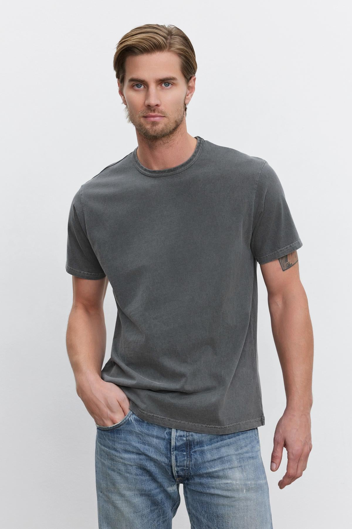   A man with short, light brown hair wearing a STITCH TEE from Velvet by Graham & Spencer and blue jeans stands against a plain white background. 