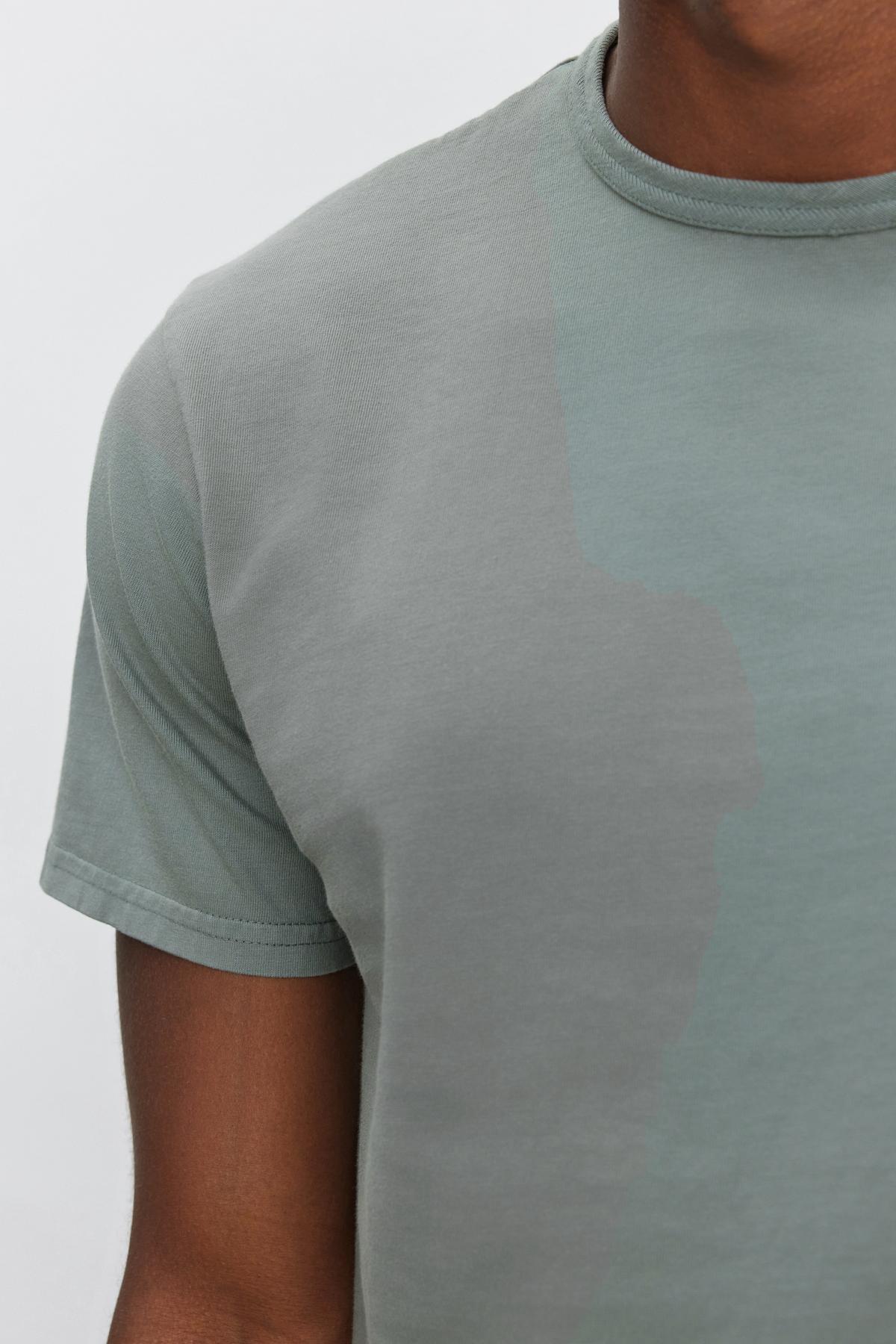   Close-up of a person wearing the STITCH TEE by Velvet by Graham & Spencer, showcasing the plain, light green, short-sleeved design with only the right shoulder and chest areas visible. 