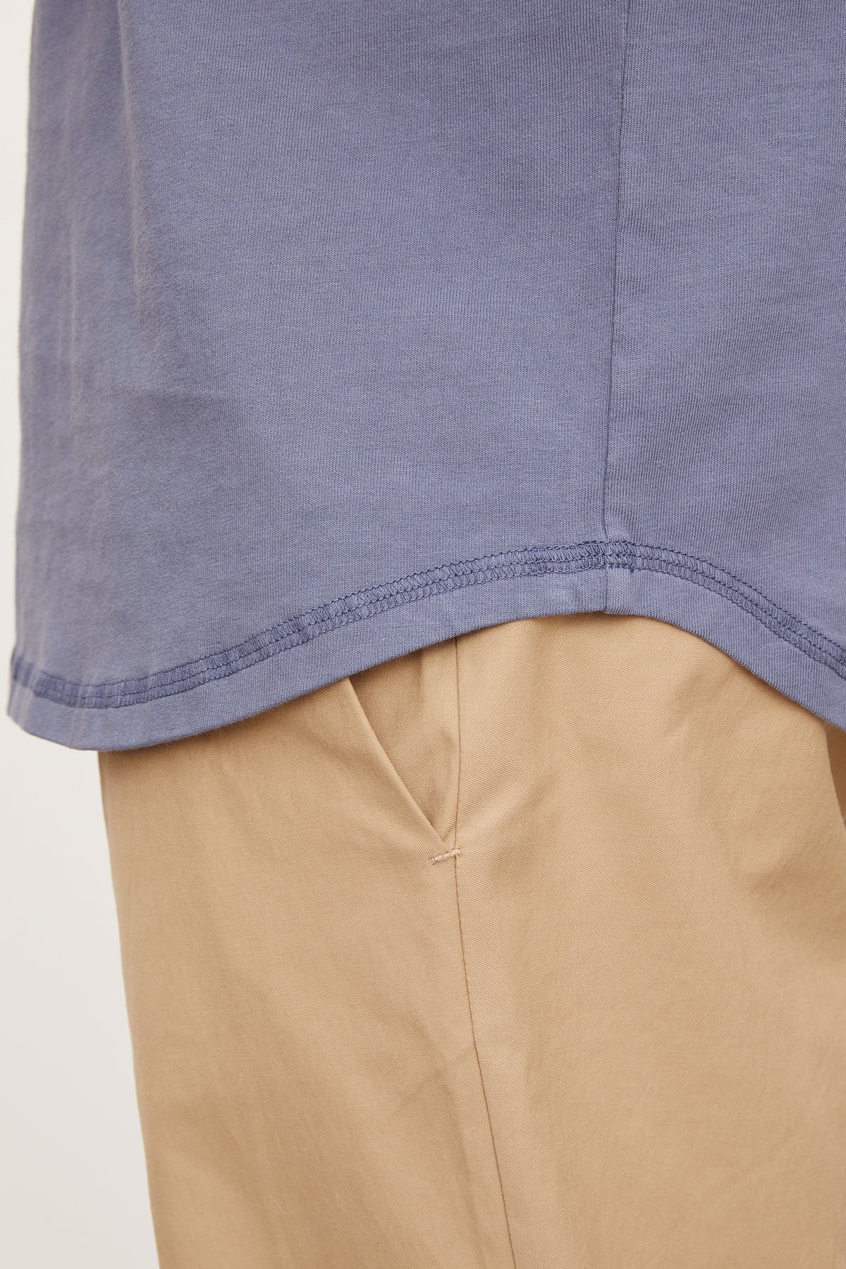   Close-up of a blue cotton knit DEON HENLEY shirt hem over beige trousers, focusing on the fabric and stitching detail by Velvet by Graham & Spencer. 