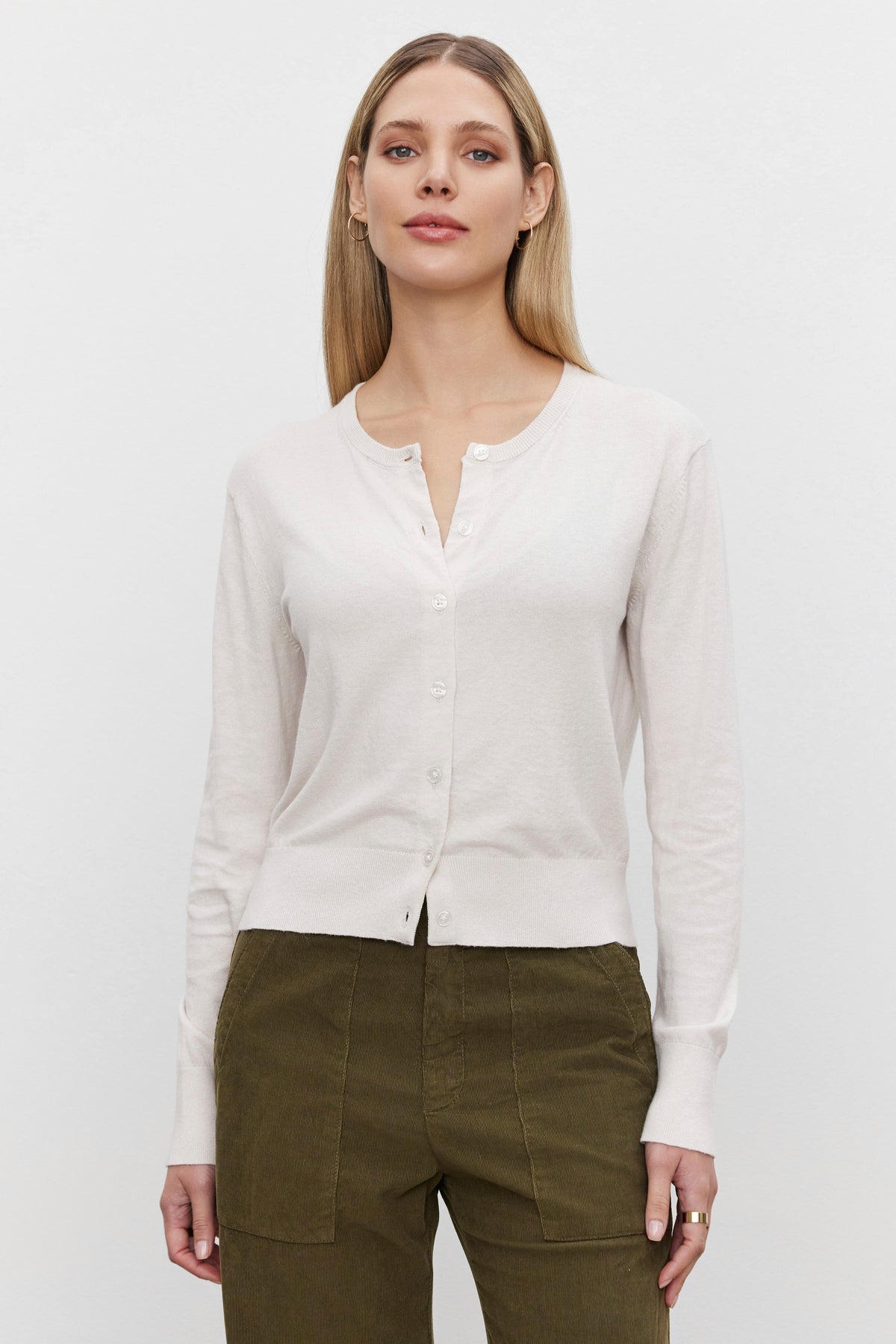   A person wearing the VIOLETTE CARDIGAN from Velvet by Graham & Spencer, made of a luxurious cotton cashmere blend, paired with olive green pants, stands against a plain white background. 