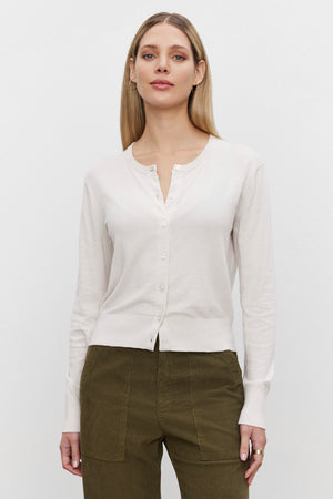 A person wearing the VIOLETTE CARDIGAN from Velvet by Graham & Spencer, made of a luxurious cotton cashmere blend, paired with olive green pants, stands against a plain white background.