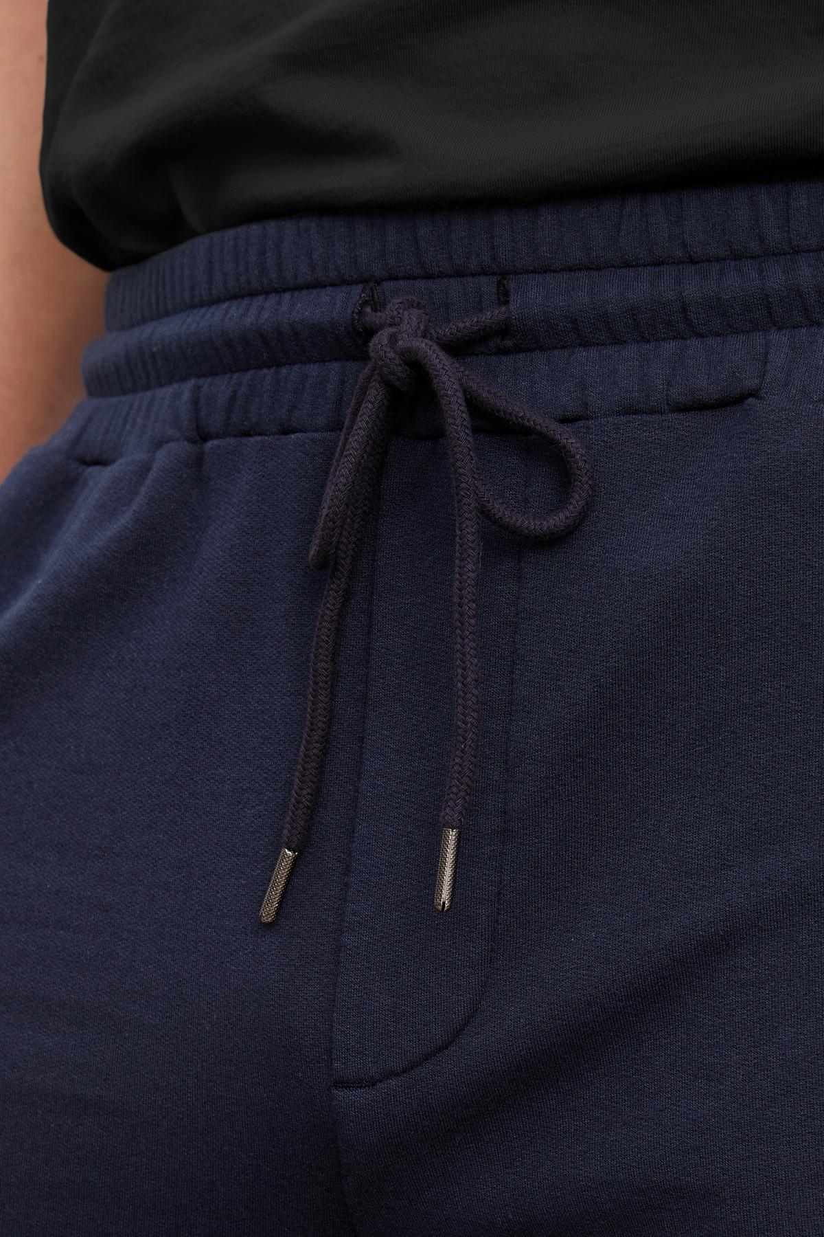   Close-up of ATLAS SHORT in navy blue, offering a tailored design with an adjustable drawstring, effortlessly paired with a black top from Velvet by Graham & Spencer. 