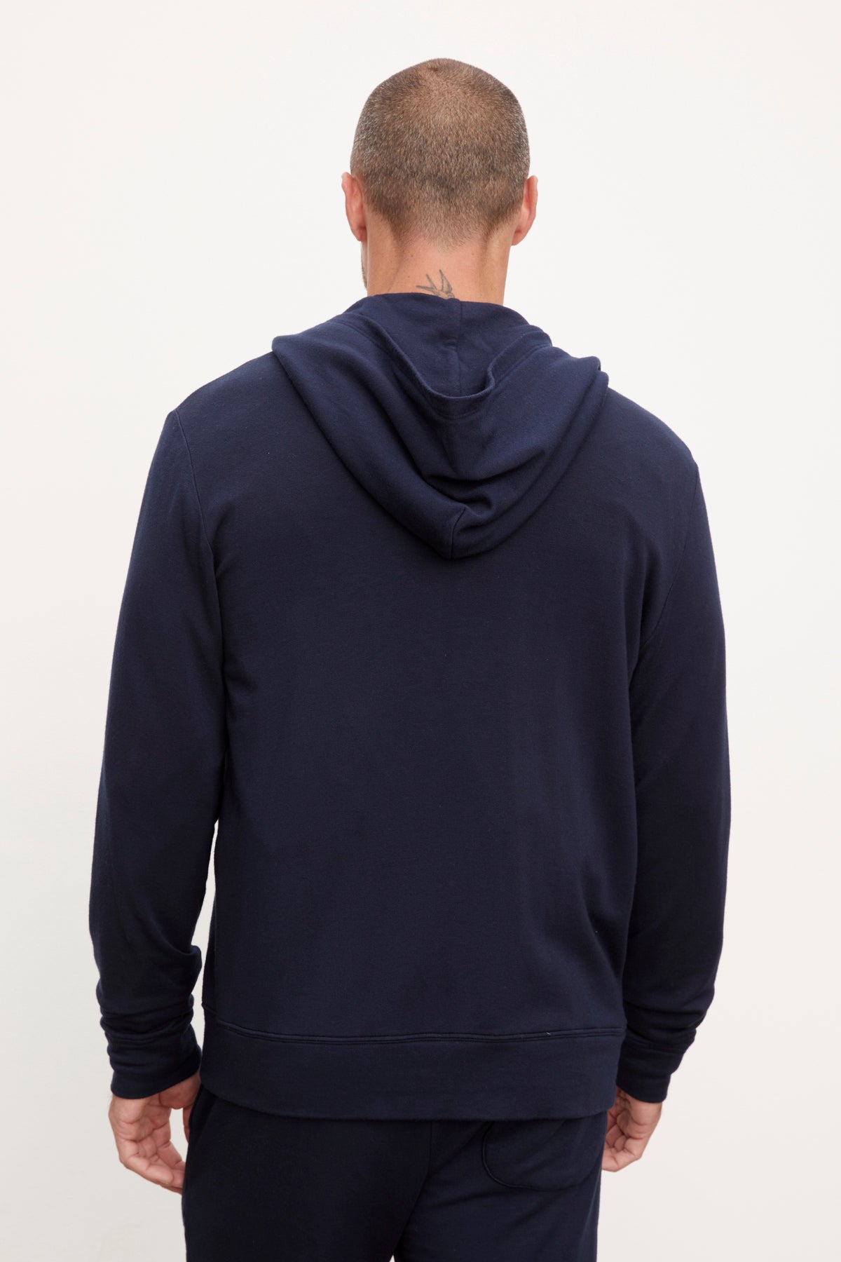   A person with a shaved head is donning the RODAN HOODIE by Velvet by Graham & Spencer in navy blue luxe fleece, facing away from the camera against a plain background. 