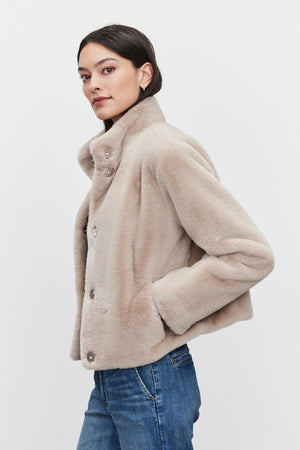 A woman wearing the SHEENA LUXE FAUX FUR JACKET by Velvet by Graham & Spencer, paired with blue jeans, stands against a plain background.