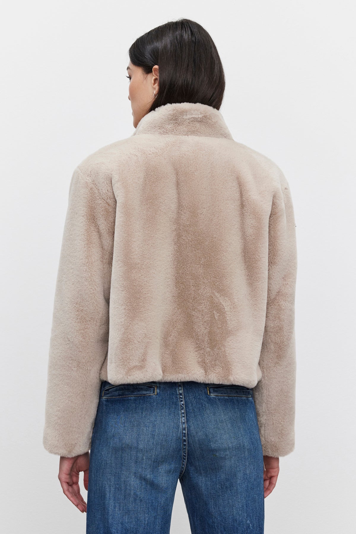   A person is seen from behind wearing the Velvet by Graham & Spencer SHEENA LUXE FAUX FUR JACKET and blue jeans, creating a stylish yet cozy look. 