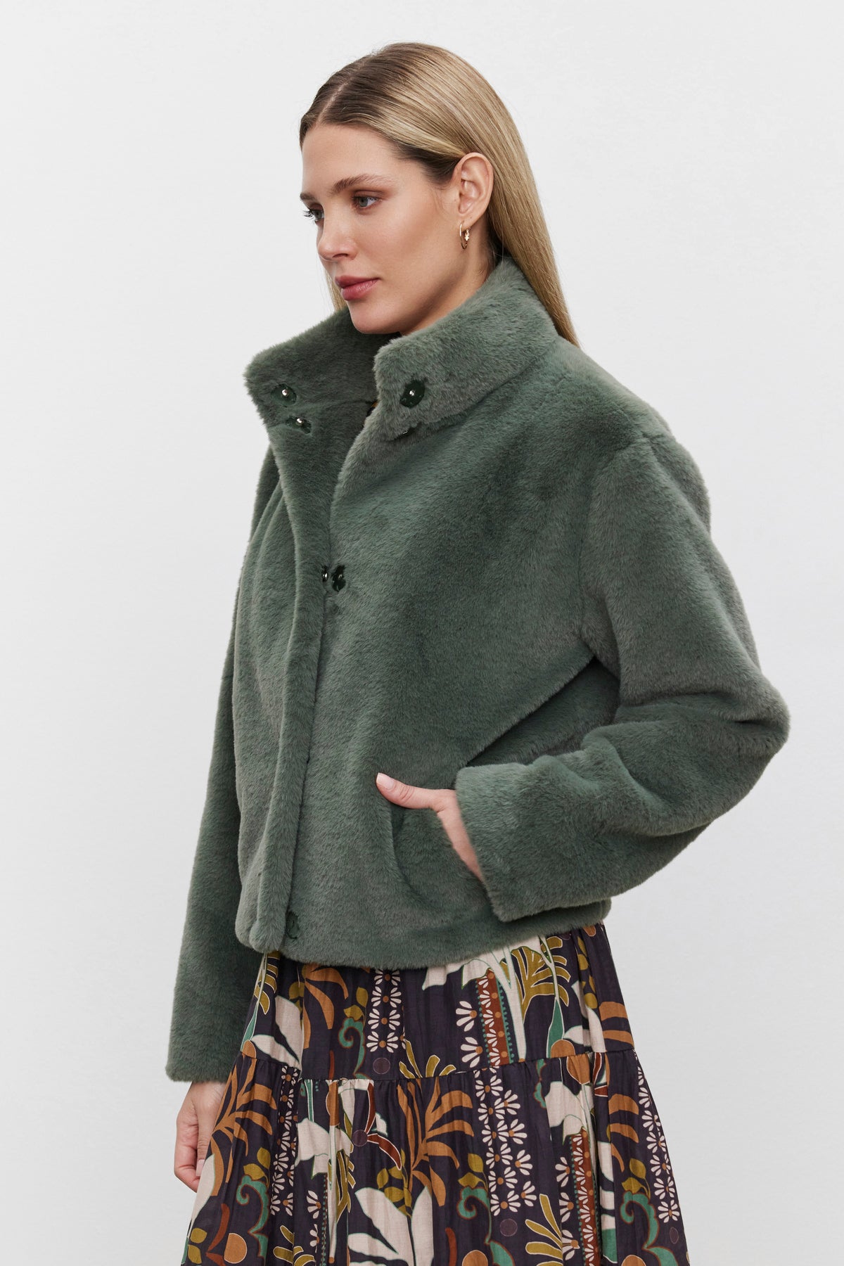   A person wearing the SHEENA LUXE FAUX FUR JACKET by Velvet by Graham & Spencer and a patterned skirt stands against a plain background. 