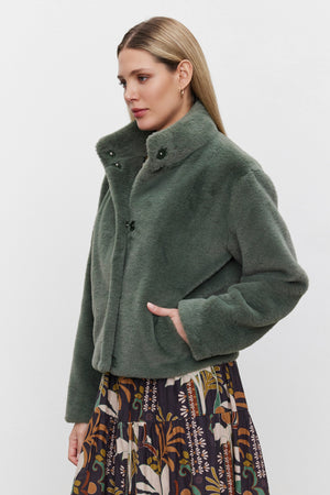 A person wearing the SHEENA LUXE FAUX FUR JACKET by Velvet by Graham & Spencer and a patterned skirt stands against a plain background.