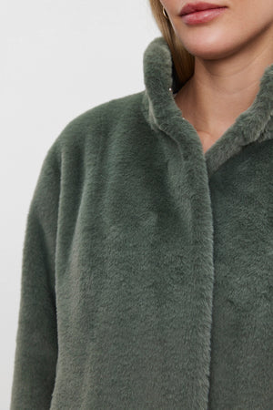 A person wearing the SHEENA LUXE FAUX FUR JACKET by Velvet by Graham & Spencer, featuring a high mock neck collar in green, partially visible from the shoulders up.