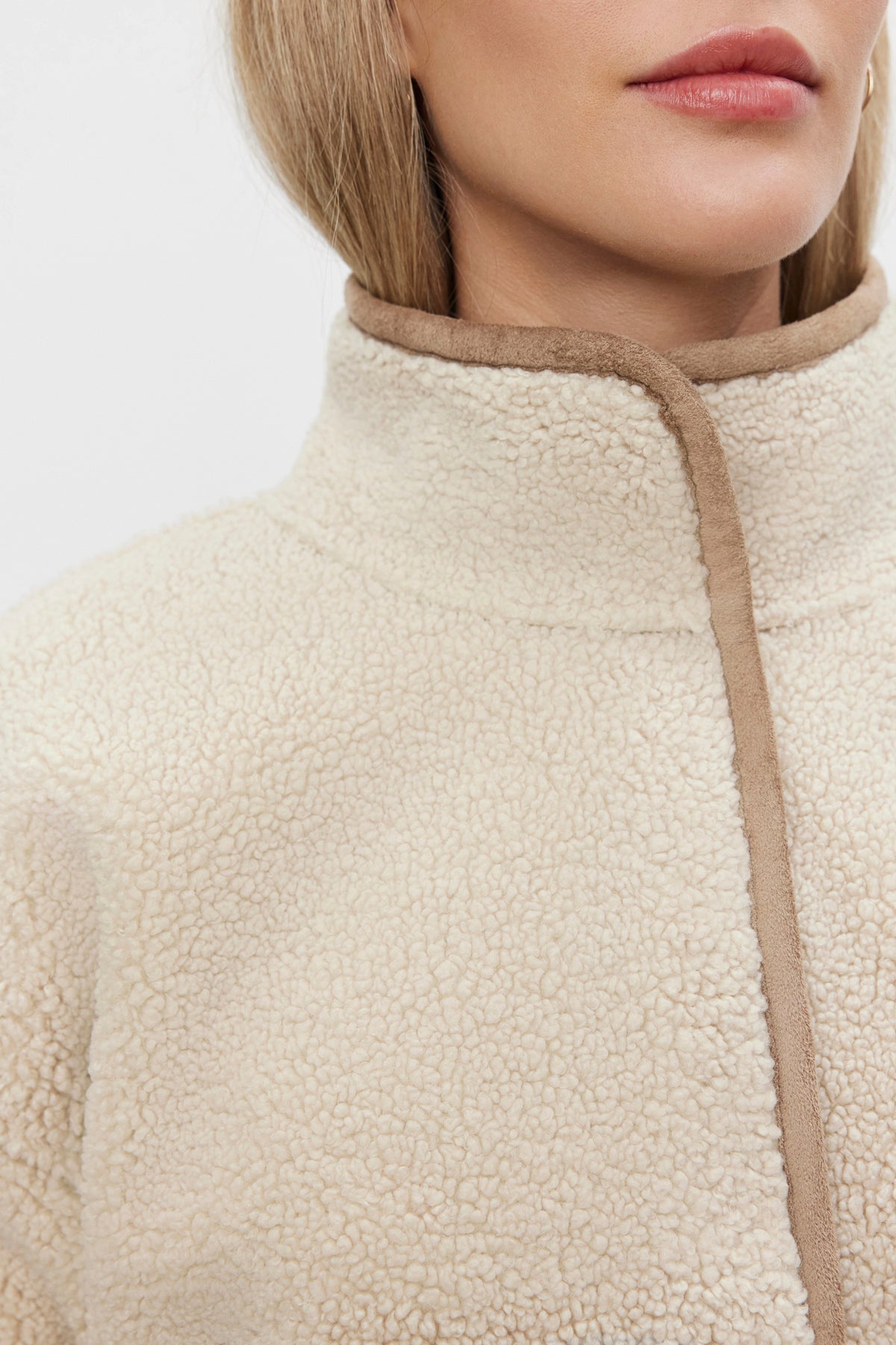   A close-up of a partially visible person wearing the ALBANY LUXE SHERPA REVERSIBLE JACKET by Velvet by Graham & Spencer, featuring an eco-friendly design in cream with brown trim and a high collar. 