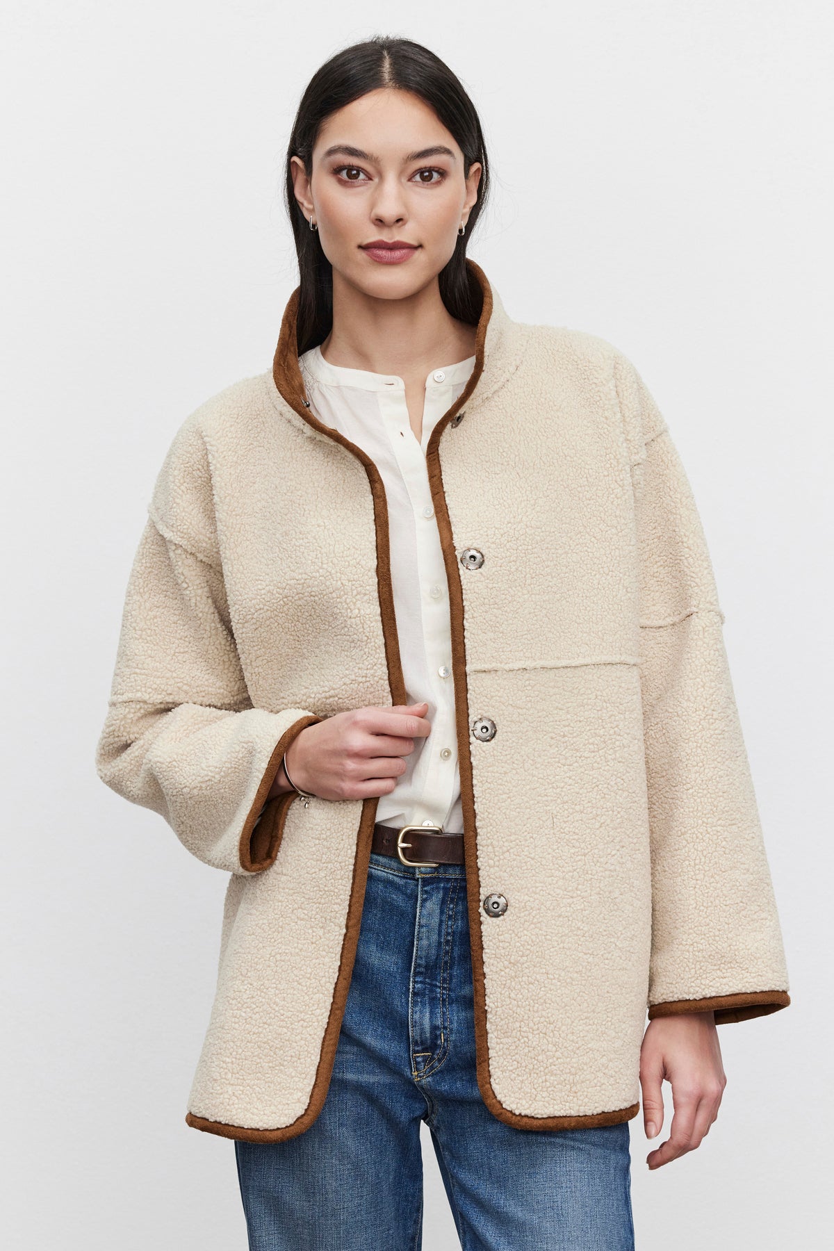 A person clad in the ALBANY LUXE SHERPA REVERSIBLE JACKET by Velvet by Graham & Spencer, featuring a cream-colored, eco-friendly faux sherpa with brown trim, stands against a plain backdrop over a white shirt and blue jeans.-37893988057281