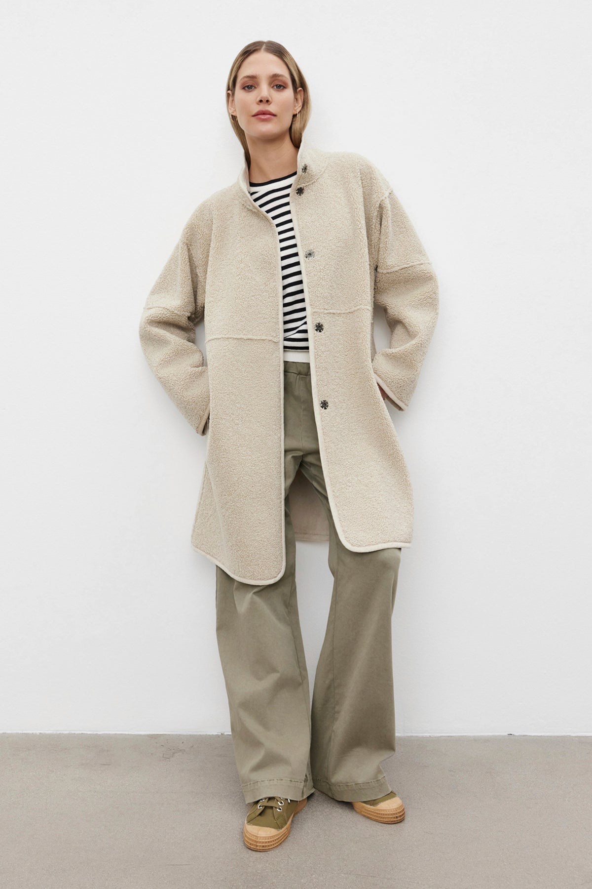   A person wearing a light beige CARA LUXE SHERPA REVERSIBLE JACKET by Velvet by Graham & Spencer over a striped shirt and khaki pants, standing against a plain background. 