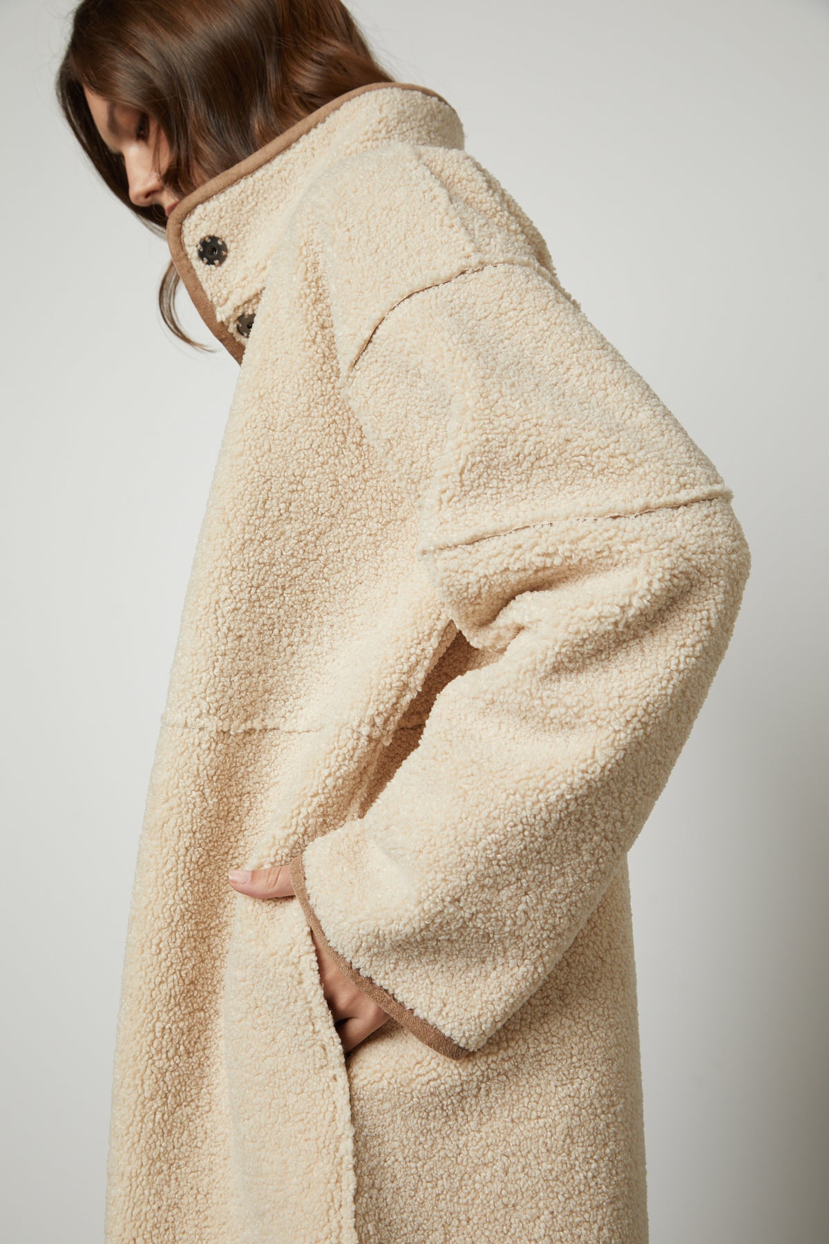   A person wearing a cream-colored, textured CARA LUXE SHERPA REVERSIBLE JACKET by Velvet by Graham & Spencer, with their hand in a pocket against a neutral background, showcasing the cozy allure of faux sherpa. 