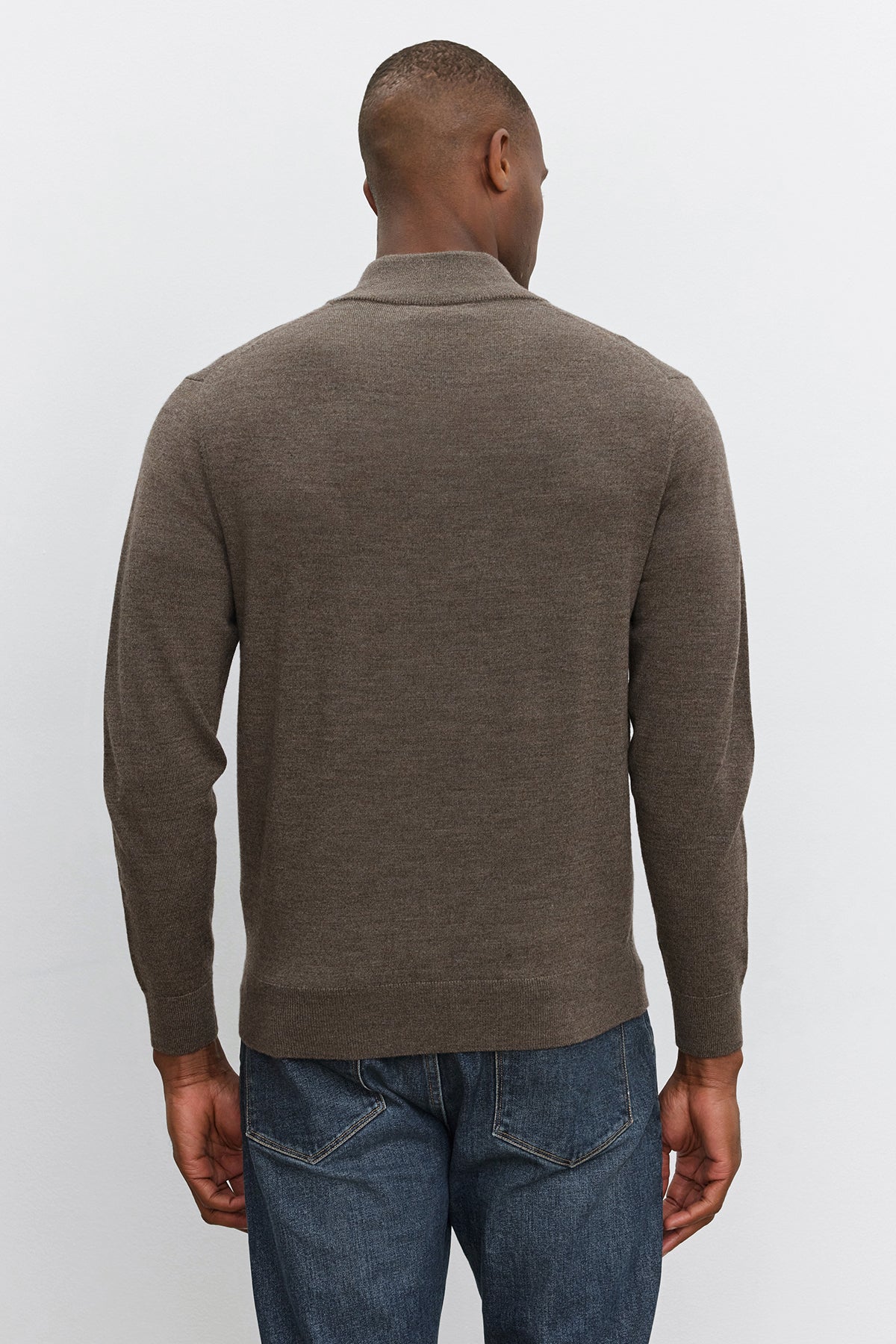   A person wearing a FLETCHER QUARTER-ZIP SWEATER in brown by Velvet by Graham & Spencer, paired with blue jeans, is shown from the back, standing against a plain white background. 