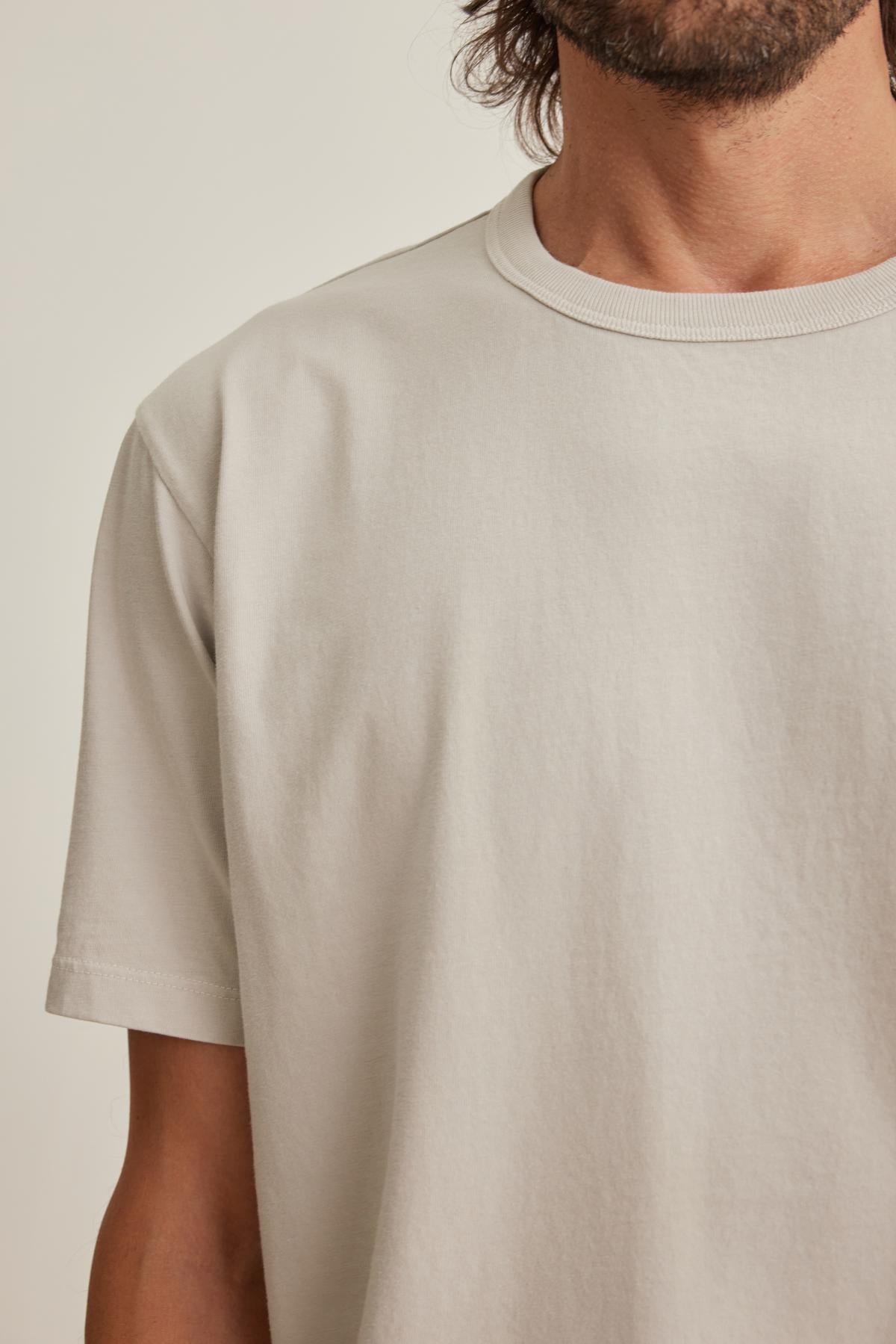   A person wearing the WELLS TEE by Velvet by Graham & Spencer, a plain light-colored shirt cropped at the shoulders and neck, standing against a neutral background. 