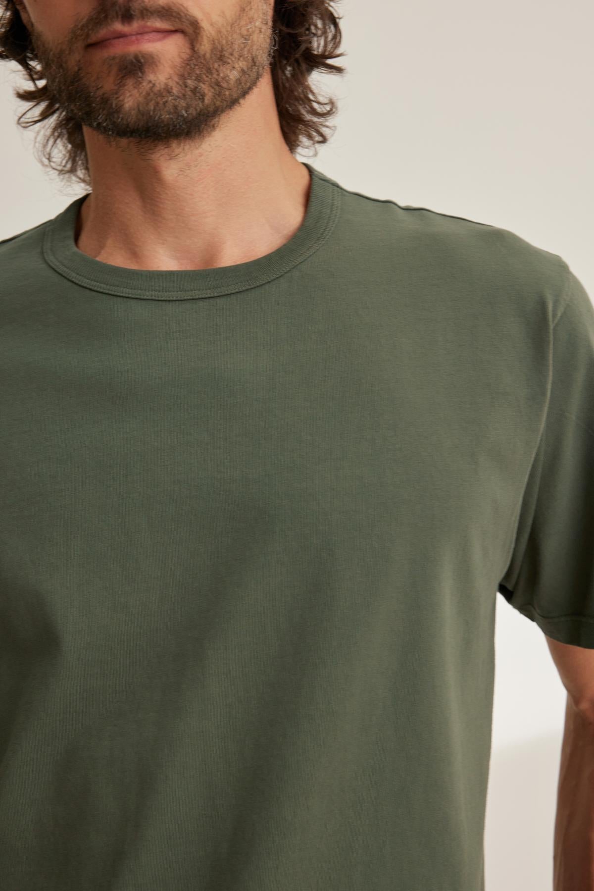   A bearded person wearing a Velvet by Graham & Spencer WELLS TEE in plain green is partially visible against a neutral background. 