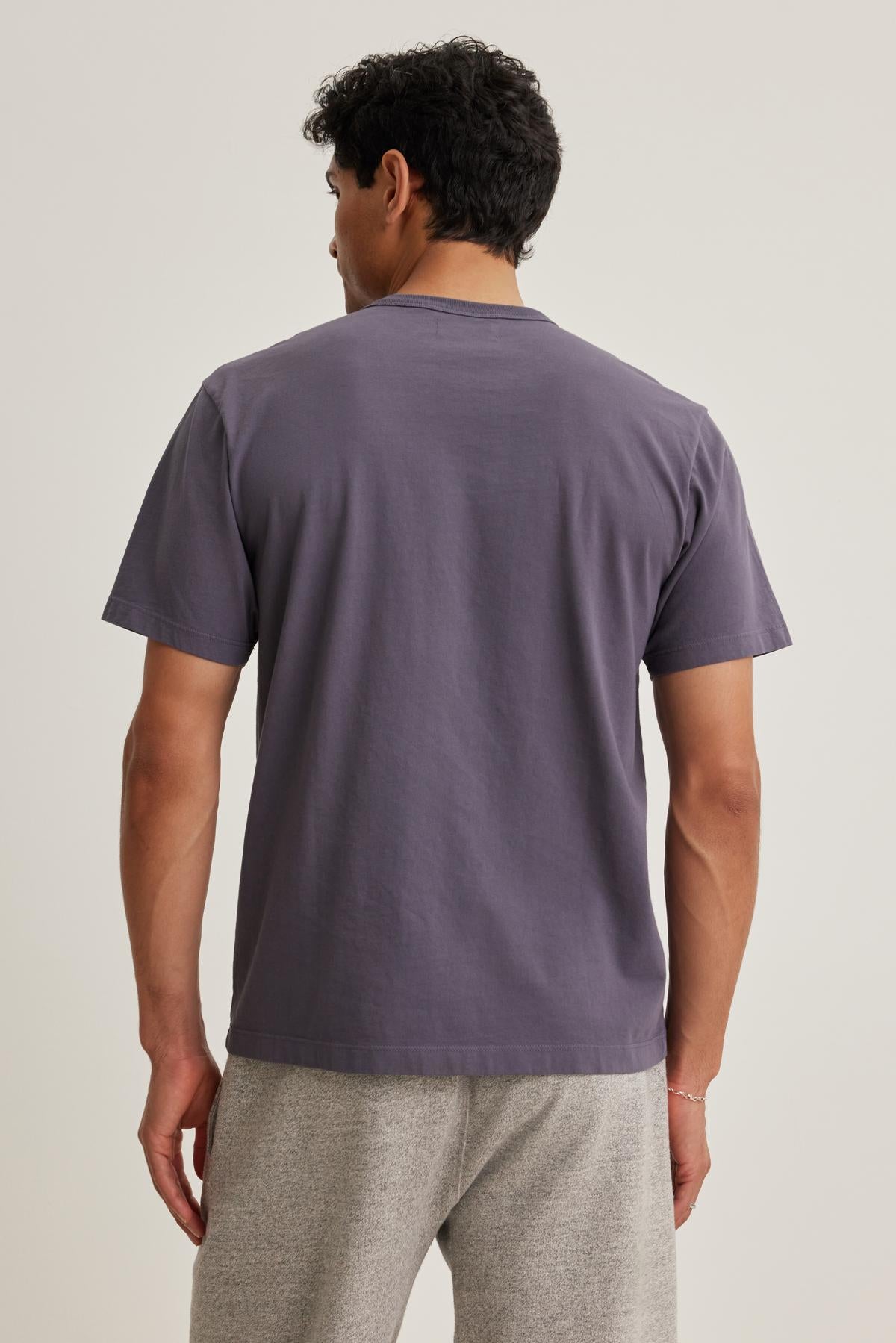   A person wearing the WELLS TEE by Velvet by Graham & Spencer and light gray pants is standing with their back to the camera. 