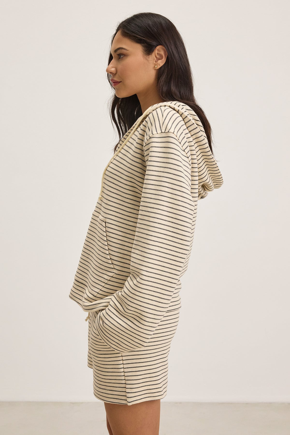   A person in a striped, mid-weight JORDYN HOODIE and shorts from Velvet by Graham & Spencer stands sideways, looking forward against a plain background. This French terry essential effortlessly combines comfort and style. 