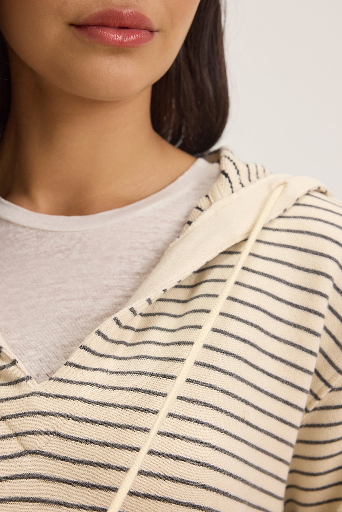   The individual is sporting the JORDYN HOODIE by Velvet by Graham & Spencer, featuring cream and black stripes made from French terry. Its relaxed neckline over a white shirt complements the look, making it a loungewear must-have. 