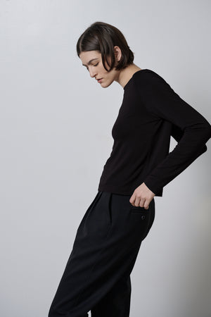 A woman wearing black trousers and a black long-sleeved top, the Velvet by Jenny Graham PACIFICA TEE in a soft hand rib knit fabric.