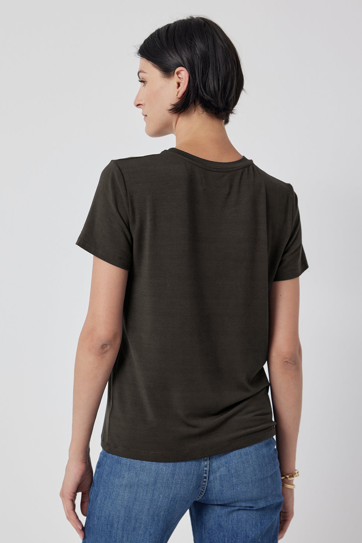   Woman wearing a plain SOLANA TEE in olive green from Velvet by Jenny Graham and blue jeans viewed from the back. 