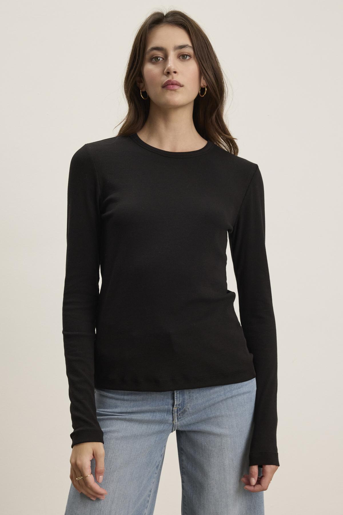 A person with long hair is standing against a plain background, dressed in the CAMINO TEE from Velvet by Jenny Graham and blue jeans, exuding a timeless appeal.-38352888791233