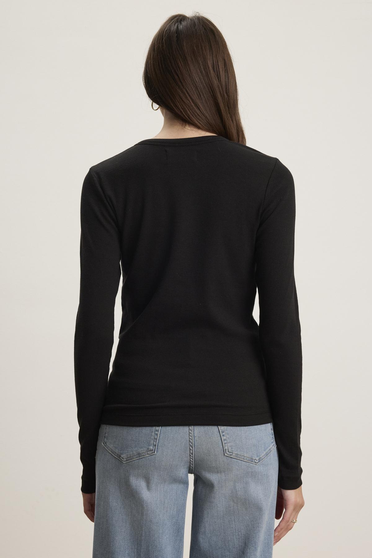   Rear view of a person wearing a timeless black Velvet by Jenny Graham CAMINO TEE and light blue slimmer fit jeans against a plain background. 