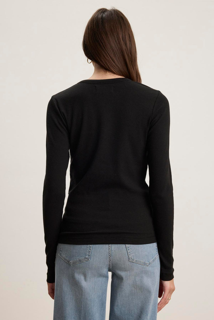 Rear view of a person wearing a timeless black Velvet by Jenny Graham CAMINO TEE and light blue slimmer fit jeans against a plain background.