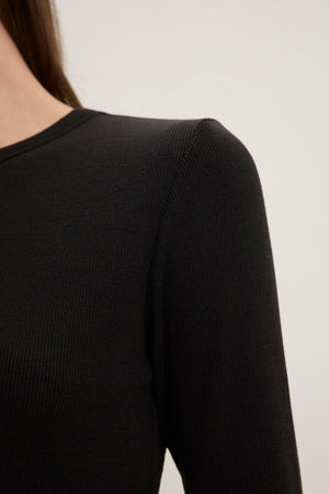 A close-up of a person wearing the Velvet by Jenny Graham CAMINO TEE, showcasing its sleek black modal rib material on the shoulder and part of the arm against a plain background. The slimmer fit enhances its timeless appeal.