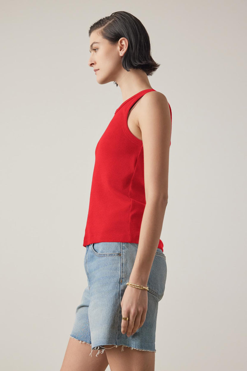 A person in the CRUZ TANK TOP by Velvet by Jenny Graham, a sleeveless red piece crafted from a ribbed cotton-modal blend, stands in profile against a plain background. This versatile top is an essential addition to any capsule wardrobe.