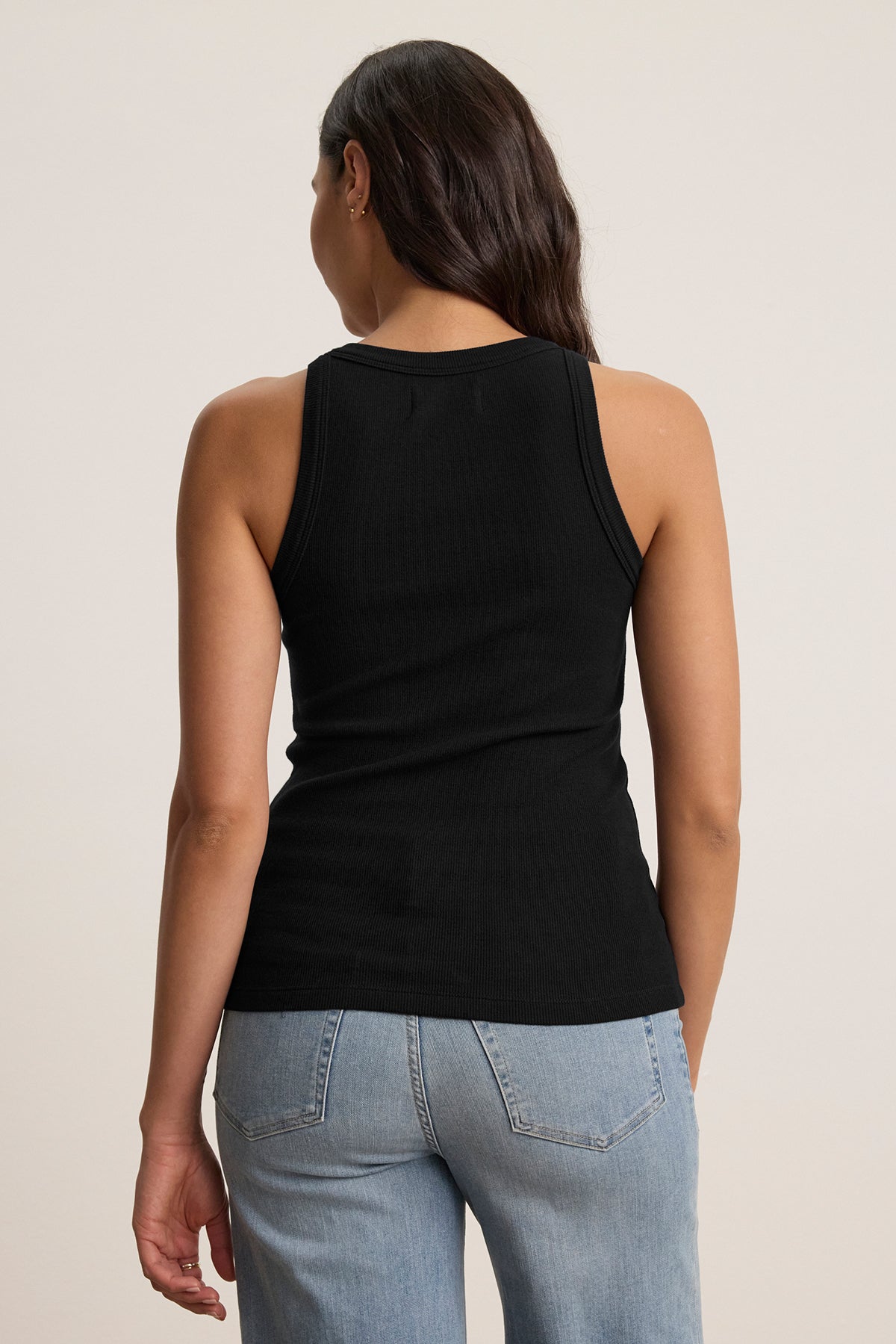   A person wearing the CRUZ TANK TOP by Velvet by Jenny Graham, a black sleeveless top crafted from a versatile cotton-modal blend, paired with light blue jeans, is facing away. 