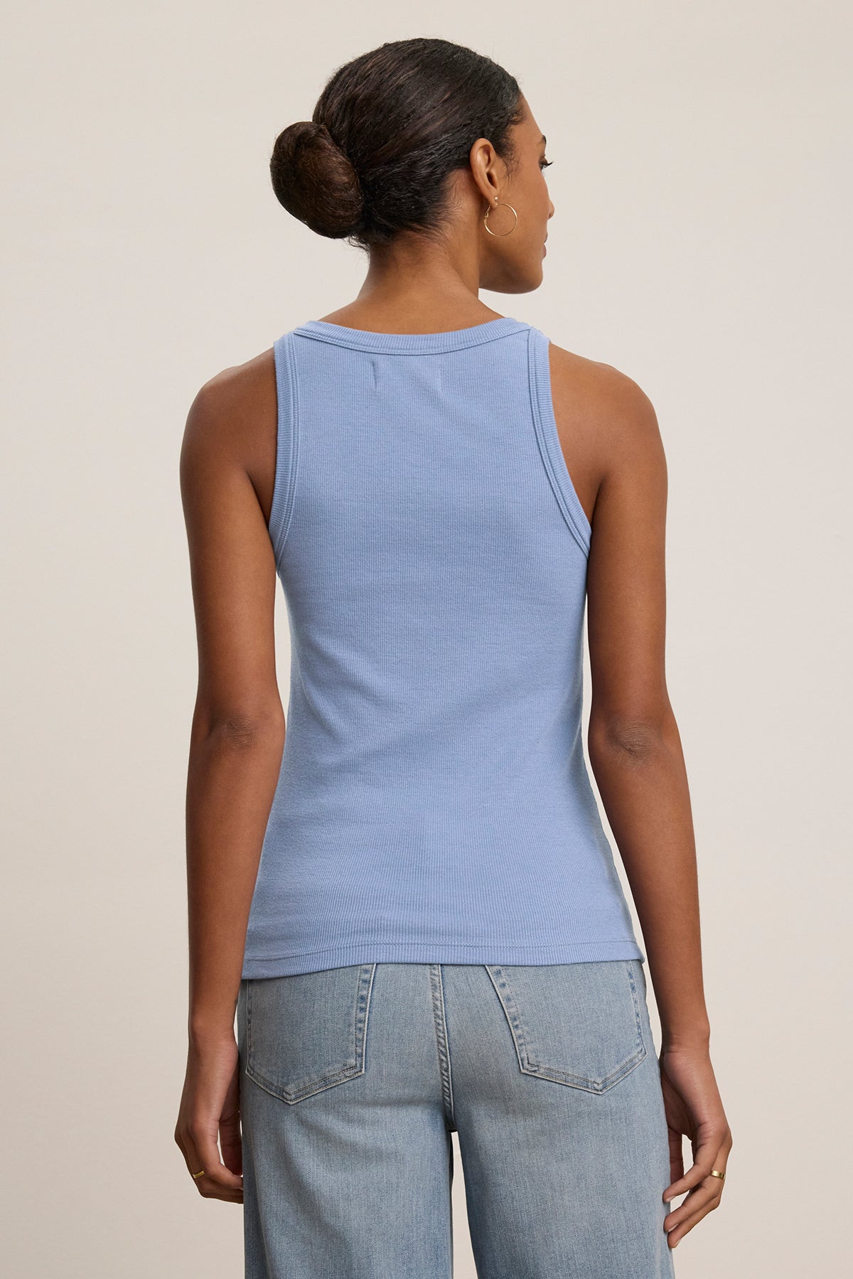 A person with a bun is seen from the back in blue jeans and the CRUZ TANK TOP by Velvet by Jenny Graham, a blue sleeveless piece crafted from a ribbed cotton-modal blend. Perfect for any capsule wardrobe, this top stands against a neutral background.-38662658457793