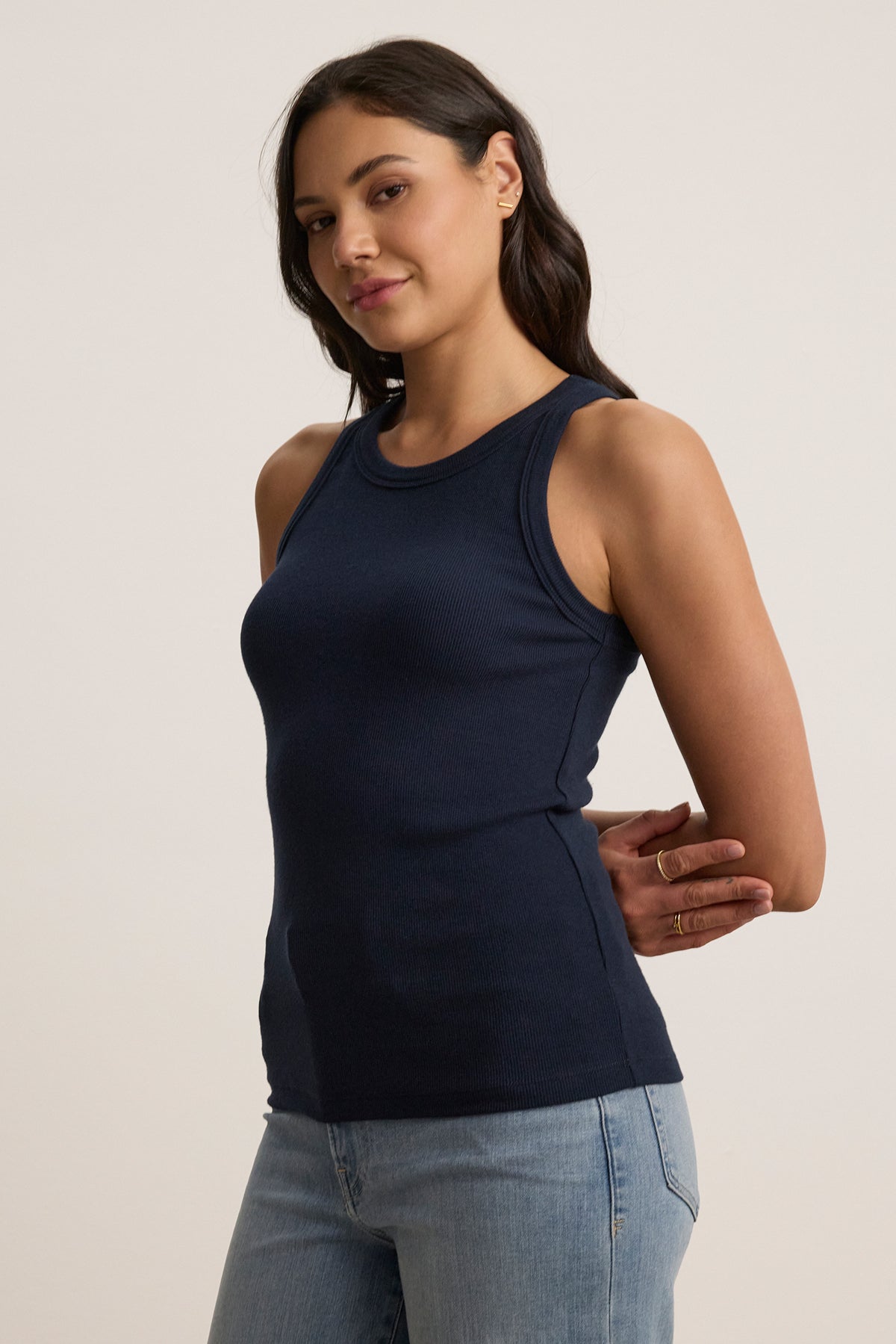 A person wearing the Velvet by Jenny Graham CRUZ TANK TOP, a sleeveless navy blue piece, paired with light jeans, stands elegantly against a neutral background—an ideal piece for any capsule wardrobe.-38662658621633