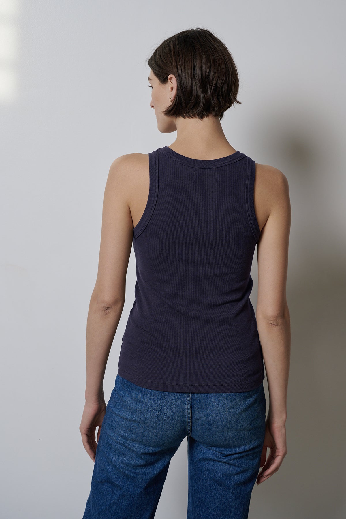   The woman's back view showcases a form-fitting CRUZ tank top by Velvet by Jenny Graham paired with jeans that offer stretch for comfort. 