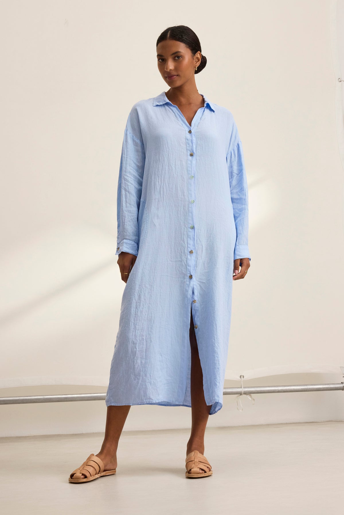 In a neutral indoor setting, someone showcases the breathable comfort and versatile design of the Velvet by Graham & Spencer NICOLE LINEN DRESS in light blue, paired with tan sandals.-38818640068801