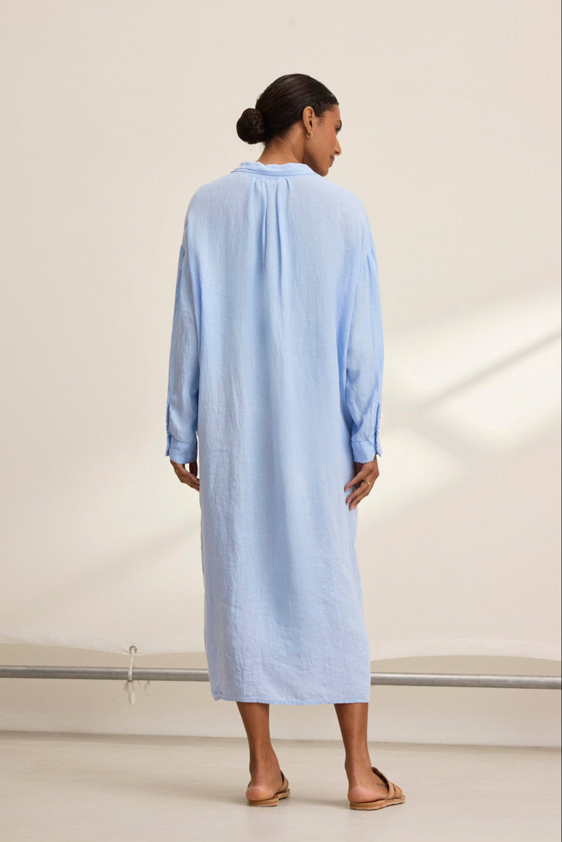   With their back to the camera, a person wears the breathable and versatile NICOLE LINEN DRESS in light blue, designed by Velvet by Graham & Spencer. 