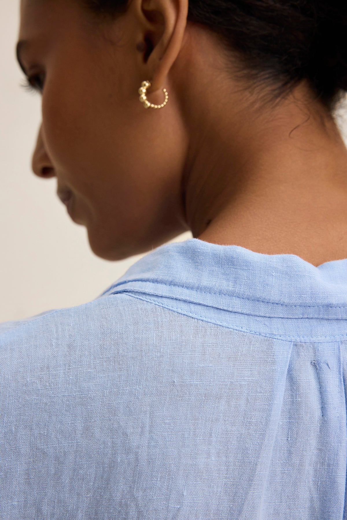   A person is shown from the back, wearing the NICOLE LINEN DRESS by Velvet by Graham & Spencer and gold hoop earrings, exemplifying versatile design and breathable comfort. 