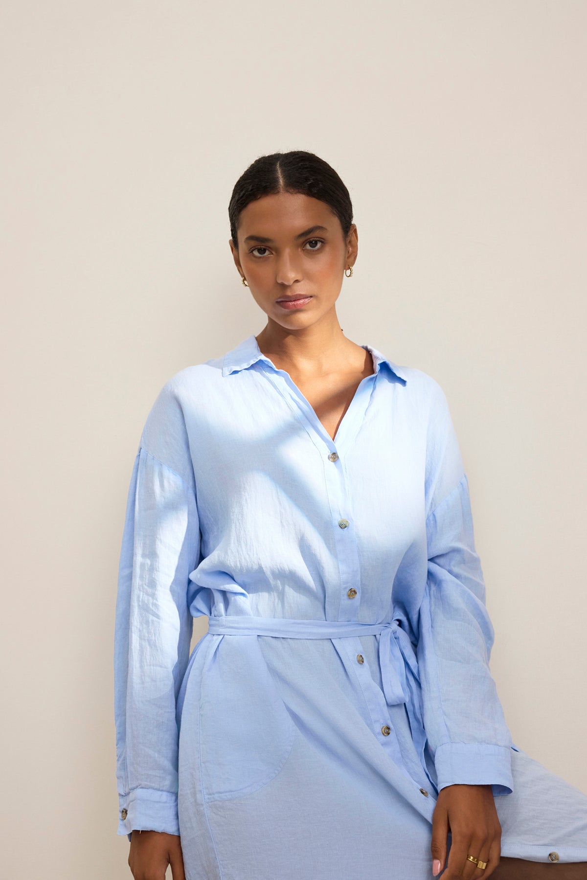 A person in a light blue NICOLE LINEN DRESS by Velvet by Graham & Spencer stands against a plain background, radiating breathable comfort.-38818640396481